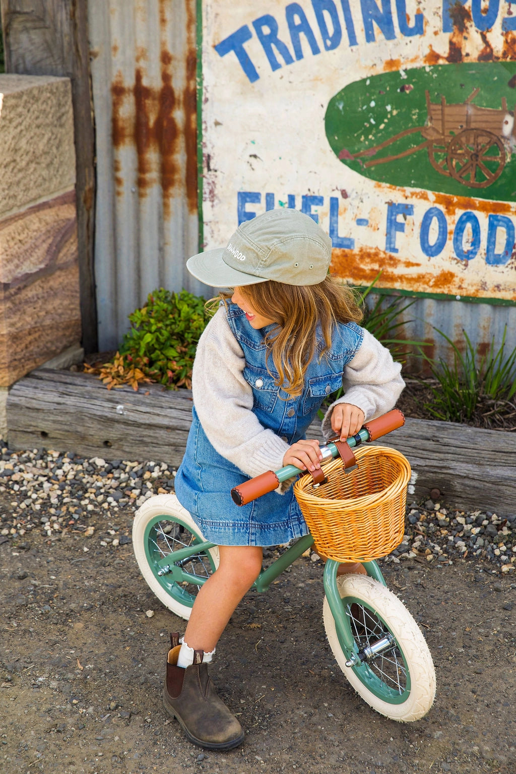 Banwood vintažinis balansinis dviratis First Go – Forest, su krepšiu ir džinsų suknele.