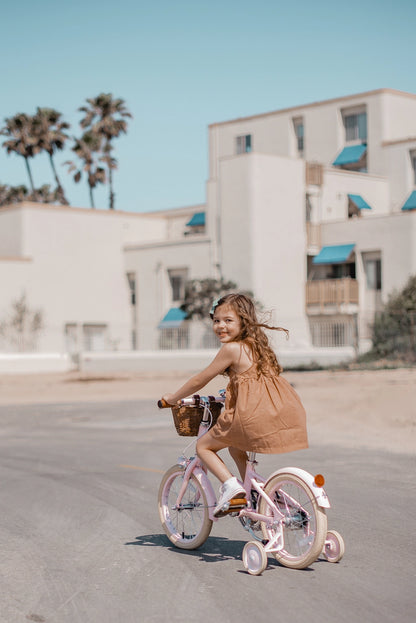 Mergaitė su Banwood 16 klasikinis vintažinis dviratis rožinės spalvos, važiuoja saulėtame kelyje.