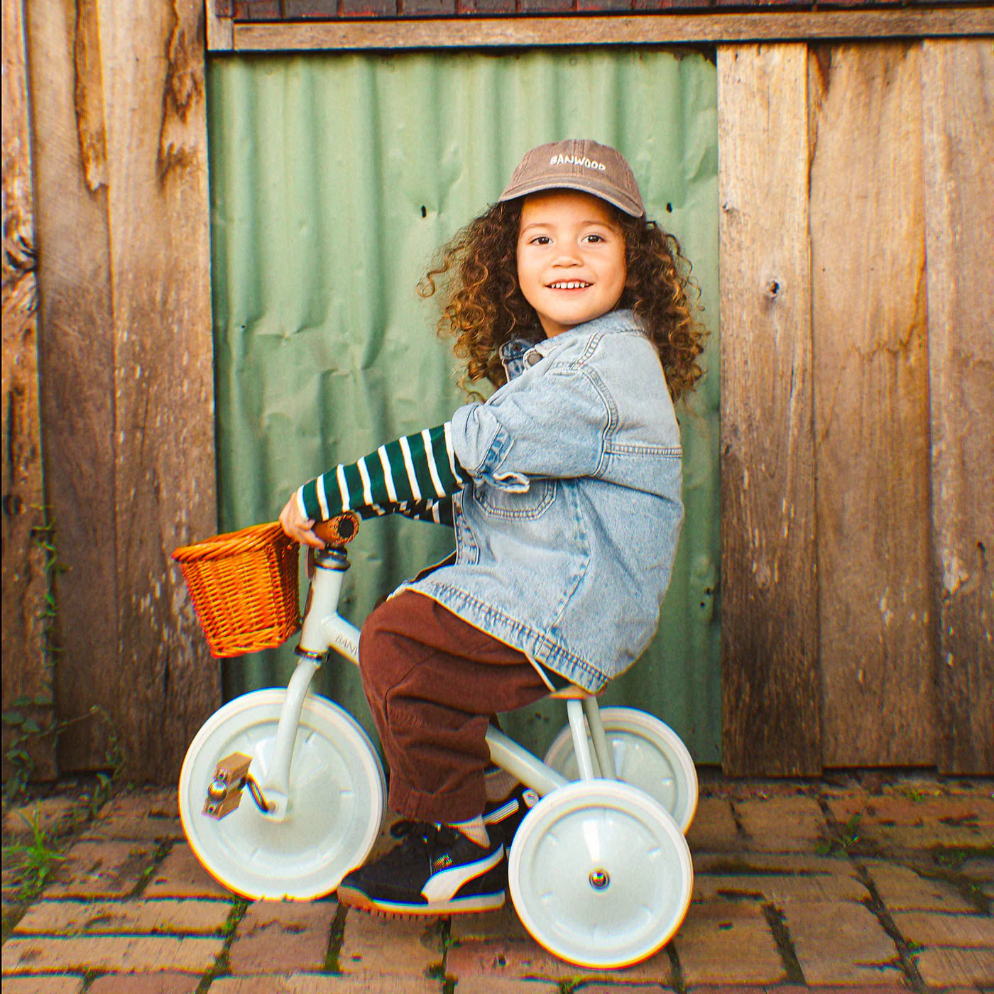 Banwood vintažinis triratukas su krepšeliu - Pale Mint, vilkėdamas mėlyną džinsinį švarką.