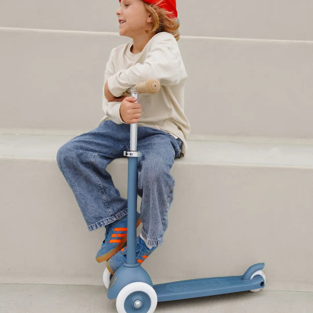 Vaikas sėdi ant Banwood vintažinis ECO paspirtukas - Deep sea, dėvintis džinsus ir šviesią palaidinę.