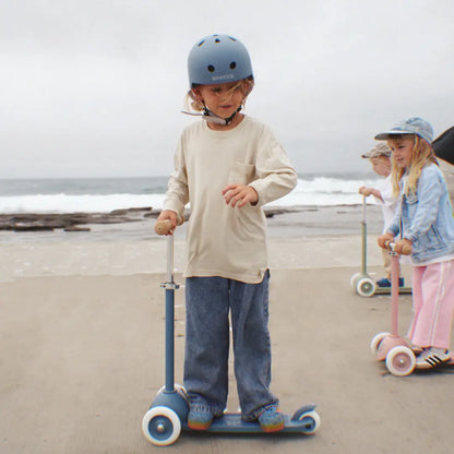 Vaikas jūroje ant Banwood vintažinis ECO paspirtukas, vilkintis šviesią marškinių ir šalmą.