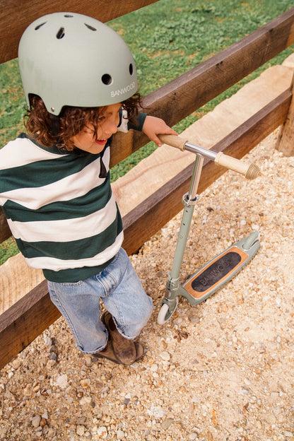 Banwood vintažinis paspirtukas su krepšeliu - Forest naudojamas vaiko lauke, kuriam uždėtas šalmukas.