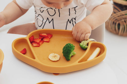 The Cotton Cloud silikoninė lėkštė su siurbtuku su maistu, skirta vaikams, laikosi ant stalo.